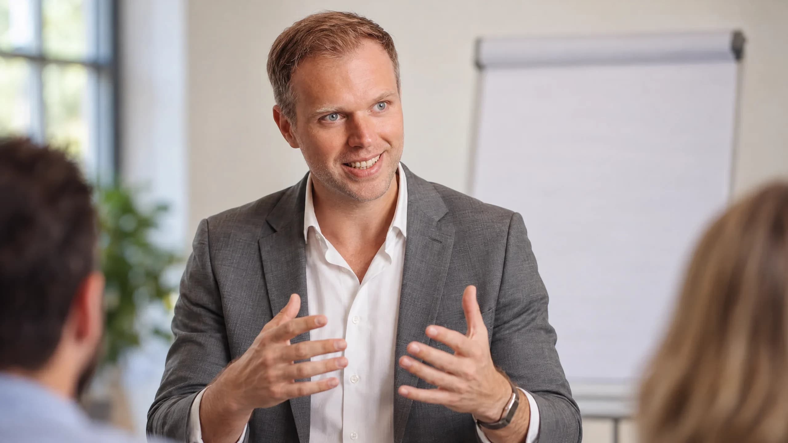 Dennis Tefett erklärt im Seminarraum mit beiden Händen etwas, hinter ihm ein Flipchart, vorn die Schultern zweier Teilnehmender