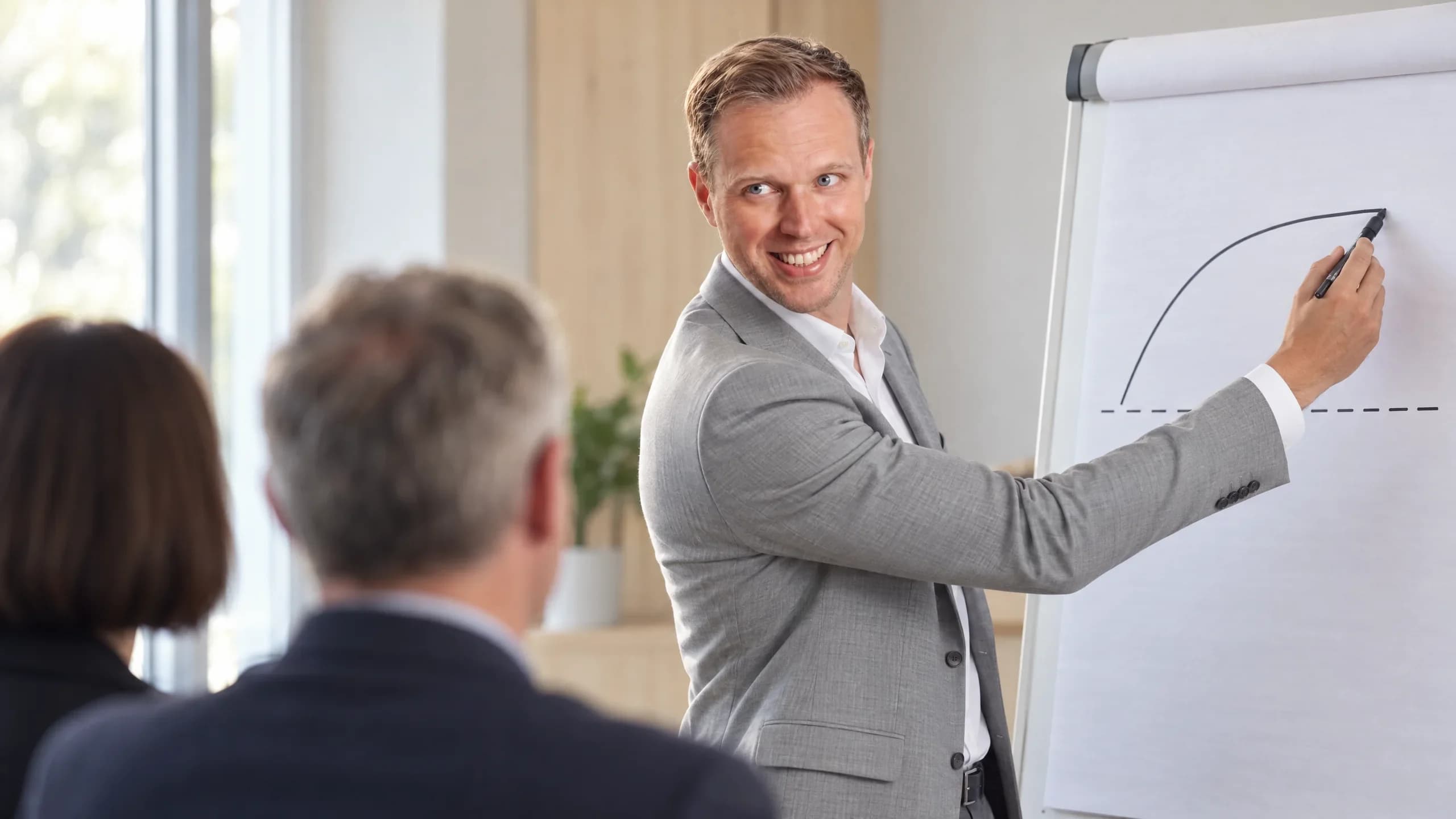 Dennis Tefett steht am Flipchart, zeichnet eine steigende Kurve und lacht seinen beiden Zuhörenden zu