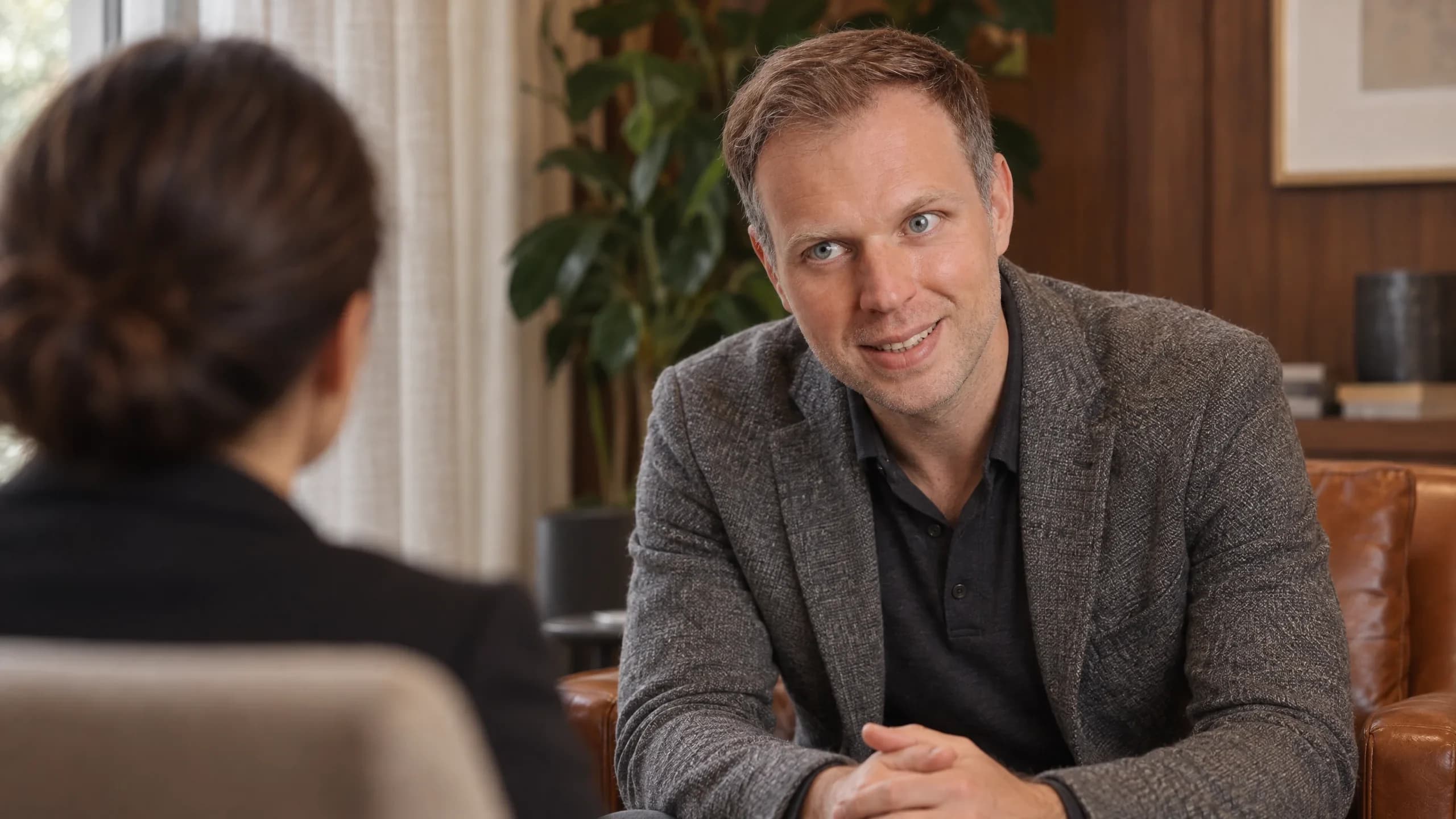 Dennis Tefett sitzt im Ledersessel seiner Praxis einer Klientin gegenüber, die Hände locker gefaltet, den Blick ruhig auf sie gerichtet