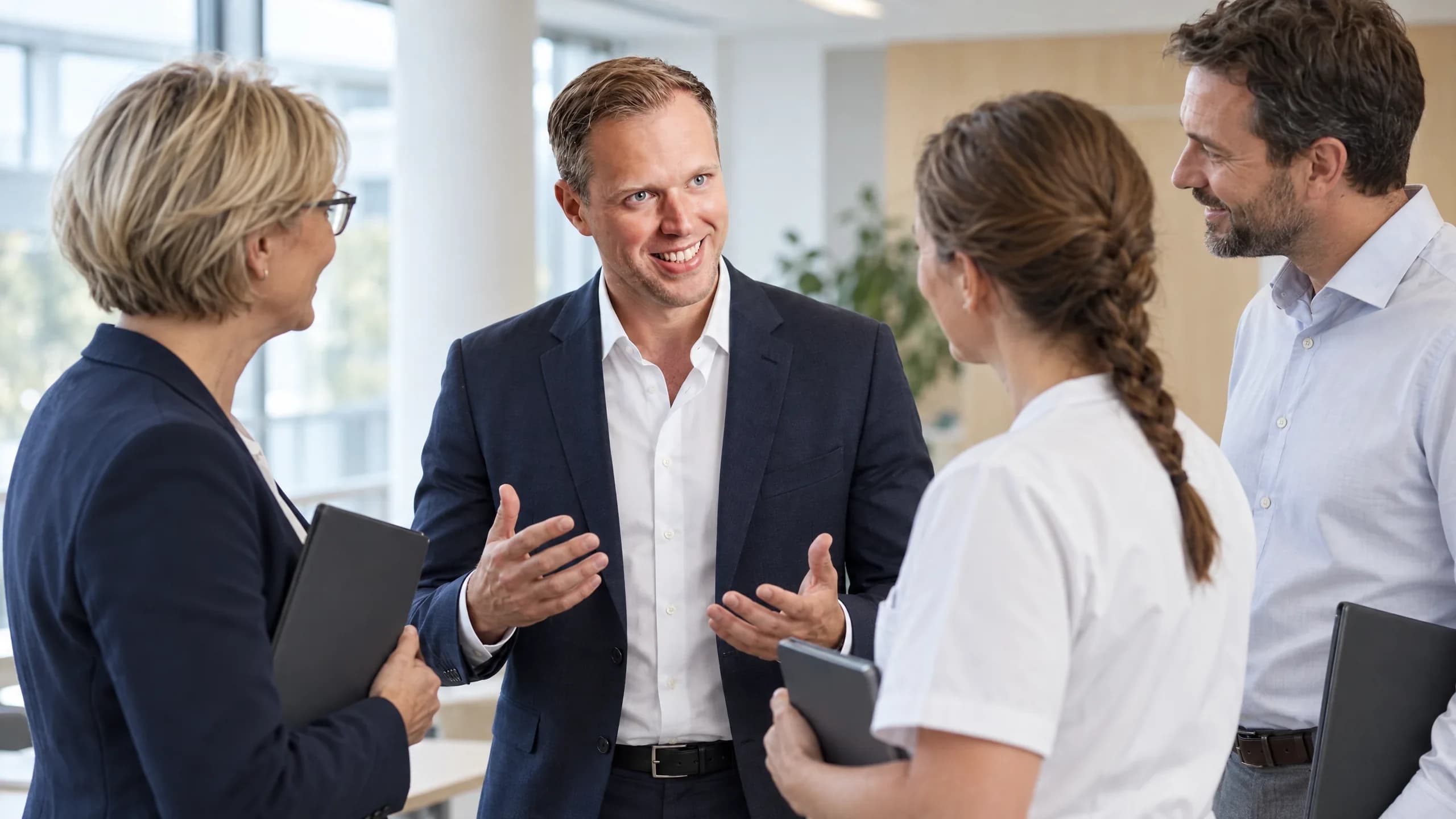 Dennis Tefett steht mit drei Leitungskräften einer Klinik zusammen, erklärt mit offenen Händen und lächelt