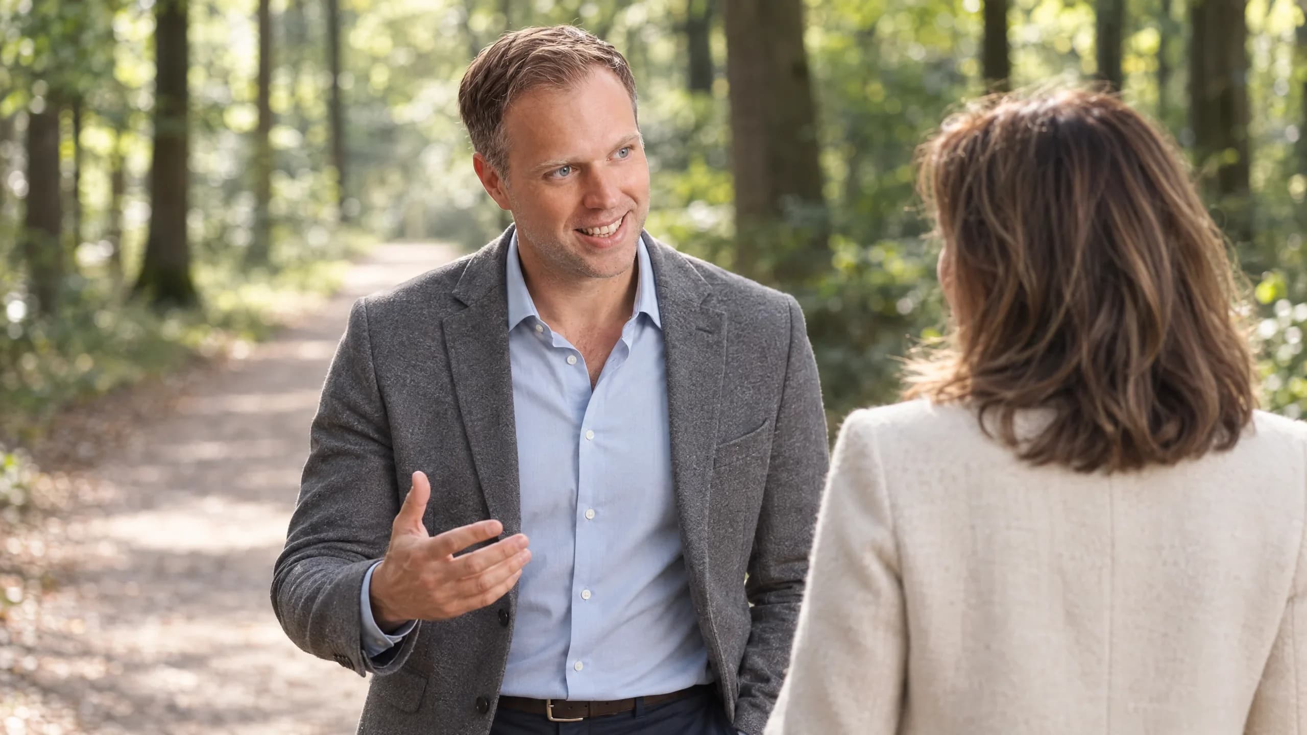 Dennis Tefett geht mit einer Klientin auf einem Waldweg und erklärt ihr im Gehen etwas mit offener Hand