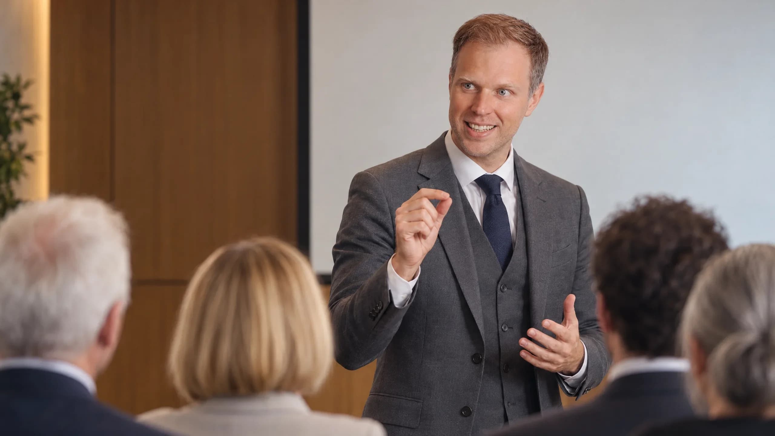 Dennis Tefett spricht im Anzug mit Krawatte vor einer sitzenden Zuhörergruppe und unterstreicht einen Gedanken mit der Hand