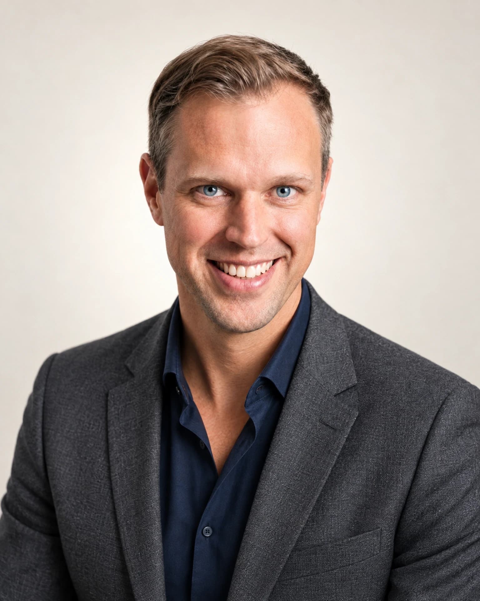 Dennis Tefett lächelt im dunkelgrauen Sakko mit dunkelblauem Hemd vor hellem Hintergrund, Arbeitsfeld Neurowissenschaften, Bottrop